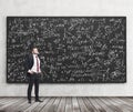 Side view of a confident young man who stands in front of black chalkboard which is full of math formulas. A concept of Analyst at