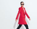 side view of cool young fashion model with sunglasses in red coat walking Royalty Free Stock Photo