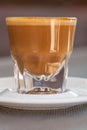 Side view of Cortado coffee in a small glass with ceramic saucer on metallic table