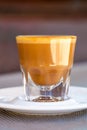 Side view of Cortado coffee in a small glass with ceramic saucer on metallic table