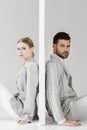 side view of couple of models in stylish jackets leaning back on sides of wall on white and looking