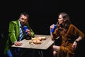 side view of couple in stylish velvet clothing sitting at table with fried onion rings french fries and sauces Royalty Free Stock Photo