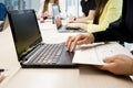 Side view of crop female working on laptop and taking notes on paper while sitting at table with group of colleagues in Royalty Free Stock Photo