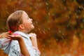 Side view of a little girl standing in the autumn park in the rain.