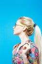 Side View of Cute Girl with Long Ponytail Wearing Colorful Shirt and Eyeglasses on Blue Background in Studio.