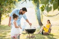 Girl watching father preparing meat on barbecue grill during family picnic
