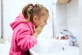 Side view of cute little girl with ponytail in pink bathrobe washing her hands. Royalty Free Stock Photo