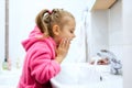 Side view of cute little girl with ponytail in pink bathrobe washing her hands. Royalty Free Stock Photo