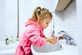 Side view of cute little girl with ponytail in pink bathrobe washing her hands. Royalty Free Stock Photo