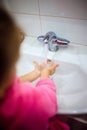 Side view of cute little girl with ponytail in pink bathrobe washing her hands. Royalty Free Stock Photo