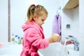 Side view of cute little girl with ponytail in pink bathrobe washing her hands. Royalty Free Stock Photo