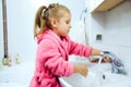 Side view of cute little girl with ponytail in pink bathrobe washing her hands. Royalty Free Stock Photo