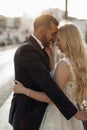 Side view of cute wedding couple standing on street with closed eyes. Young woman bride embracing with groom in suit.