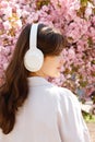 Side View of the Cute Young Girl with Freakles Standing and Looking Away Wearing Big White Headphones on the Blooming Royalty Free Stock Photo