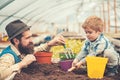 Side view daddy looking at his lovely boy playing with soil. Hipster with stylish beard in fedora hat helping his son