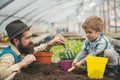 Side view daddy looking at his lovely boy playing with soil. Hipster with stylish beard in fedora hat helping his son