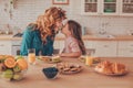 Side view of daughter and mother touching noses while sitting at the kitchen table with food Royalty Free Stock Photo