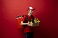 Side view delivery man in red uniform on a red background delivering food, groceries, vegetables, drinks in a paper box Royalty Free Stock Photo