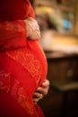 Side view of Detail of pregnant woman with red dress with hands on belly