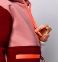 Side view detail of stylish girl sport coat colored in red, pink and white. Hand of model holding hoodie string.