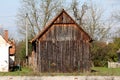 Side view of dilapidated old vintage rustic wooden barn with cracked wooden boards and leaning roof next to abandoned family house Royalty Free Stock Photo