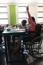 Side view of disable schoolgirl raising hand and sitting at desk in classroom