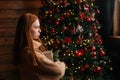 Side view of dissatisfied young woman holding Christmas gift box on background of xmas tree. Royalty Free Stock Photo