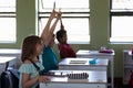 Group of school children sitting at desks and raising their hands to answer Royalty Free Stock Photo