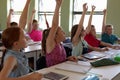 Group of school children sitting at desks and raising their hands to answer Royalty Free Stock Photo