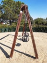 Side view of double swing bench with metal ropes on sand ground of playground. Closeup of empty swing on children playground.