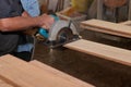 Side view of electric circular saw is being cut a piece of wood against hands of senior carpenter in carpentry workshop. Royalty Free Stock Photo