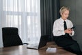 Side view of elegant middle-aged business woman using typing smartphone searching info sitting on office desk. Female Royalty Free Stock Photo