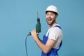 Side view excited young man in coveralls protective helmet hardhat hold electric drill isolated on pastel blue