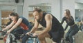 Side view of exhausted perspiring man riding fast on exercise bike and ending exercise. Handsome Caucasian brunette