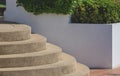 Side view of exposed aggregate finish cobblestone round staircase with green bush on white concrete fence wall decoration