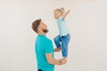 Side view of family wearing blue T-shirts, jeans. Little girl with short fair hair standing on man hands, raising hands. Royalty Free Stock Photo