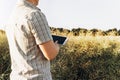 Side view of farmer standing in field at sunset, using tablet to assess the state of agricultural crop. Modern technologies