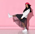 Side view of a little Korean girl model posing in the studio on a pink background raising her leg.