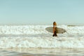 Side view of female surfer in wetsuit with his surfboard entering the sea. Surfing on waves Royalty Free Stock Photo