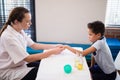 Side view of female therapist examining hand while boy sitting at table Royalty Free Stock Photo