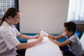 Side view of female therapist wrapping bandage on hand while boy sitting at table Royalty Free Stock Photo