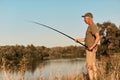 Side view of fisher standing on bank of lake or river and looking at his fishing rod in hands, fishing on sunset, at beautiful Royalty Free Stock Photo
