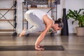 Strong man performing crane pose on mat in yoga studio