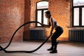 Side view of fitness young athletic woman with strong beautiful body in black sportswear exercising with battle ropes Royalty Free Stock Photo