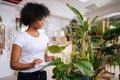 Side view of focused African American young woman in white shirt carefully wiping dust with soft cloth from leaves of