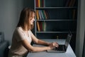 Side view of focused business woman working on laptop computer from home office sitting at desk in dark room. Royalty Free Stock Photo