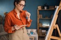 side view focused ethnic woman in casual clothes stands near the canvas holds a palette with paints in her hands looks Royalty Free Stock Photo