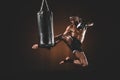 Side view of focused muay thai fighter practicing kick on punching bag