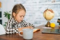 Side view of focused primary child school girl doing writing homework sitting at table with laptop and paper notebook at Royalty Free Stock Photo