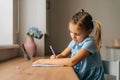 Side view of focused primary little child girl learning writing doing homework sitting at home table by window. Royalty Free Stock Photo